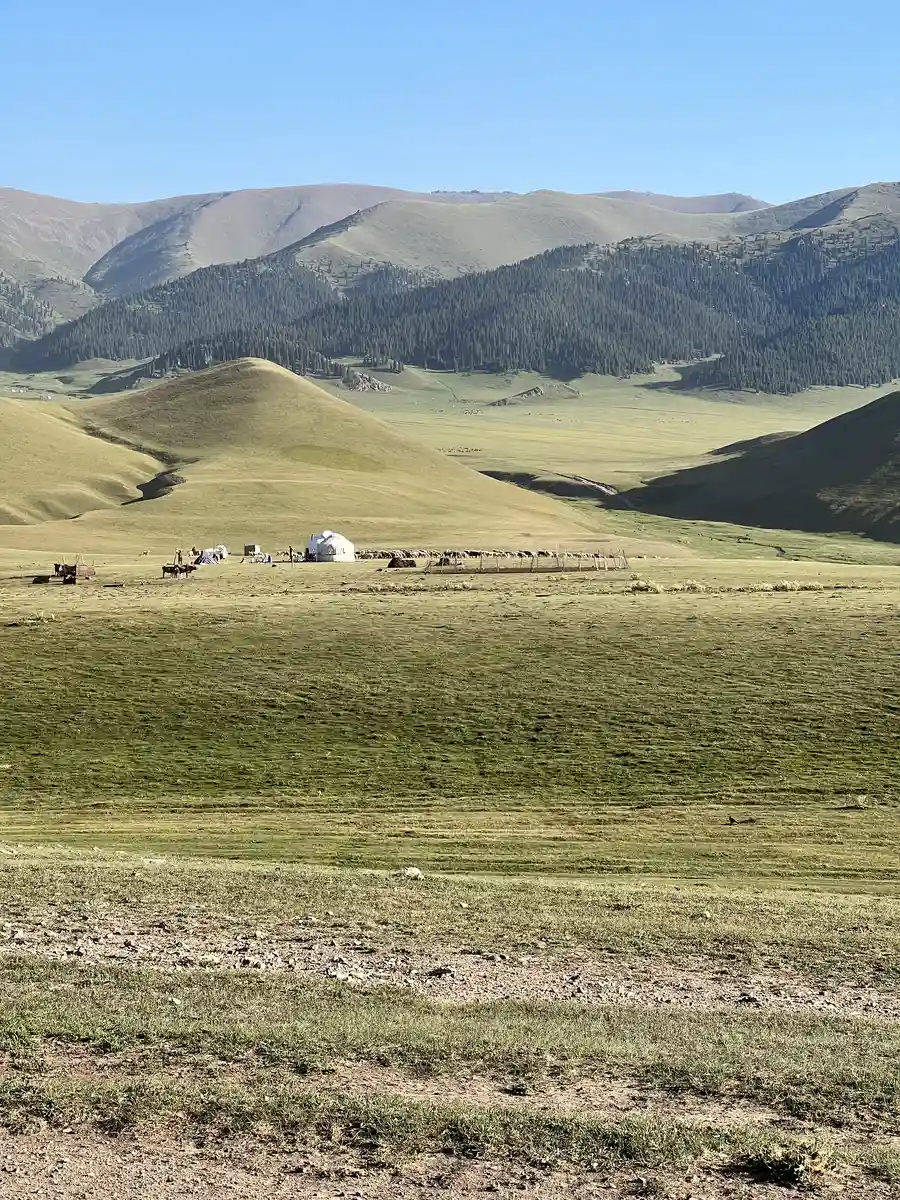 White yurt camp set in the wide green steppe of the Assy Plateau surrounded by rolling hills